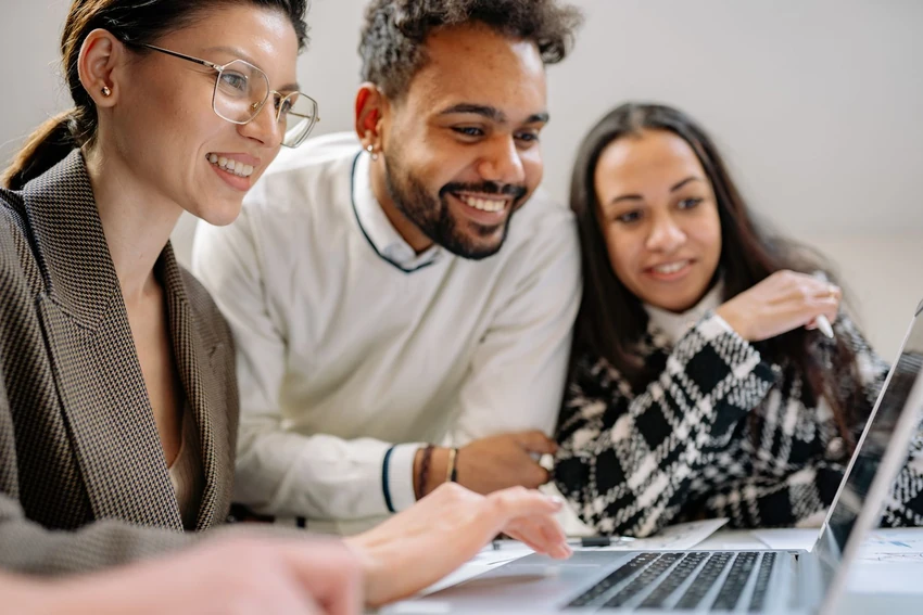 Three colleagues smiling while reviewing keyword research on a laptop