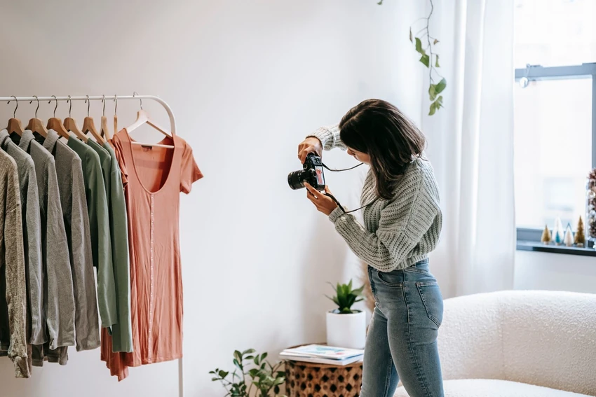 A photographer taking a picture of clothes displayed on hangers beside a bright window